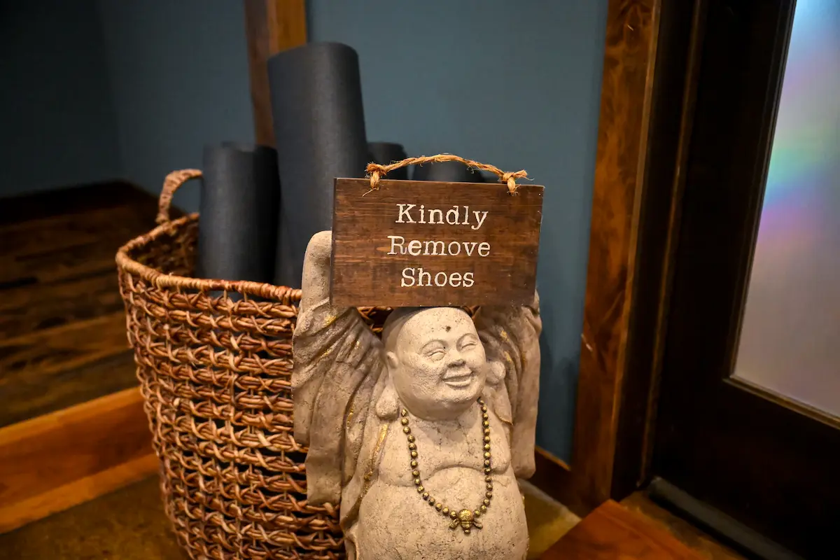 Sign on basket with yoga mats inside: Kindly Remove Shoes