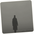 Silhouette of a person in a long coat standing in foggy, gray surroundings.