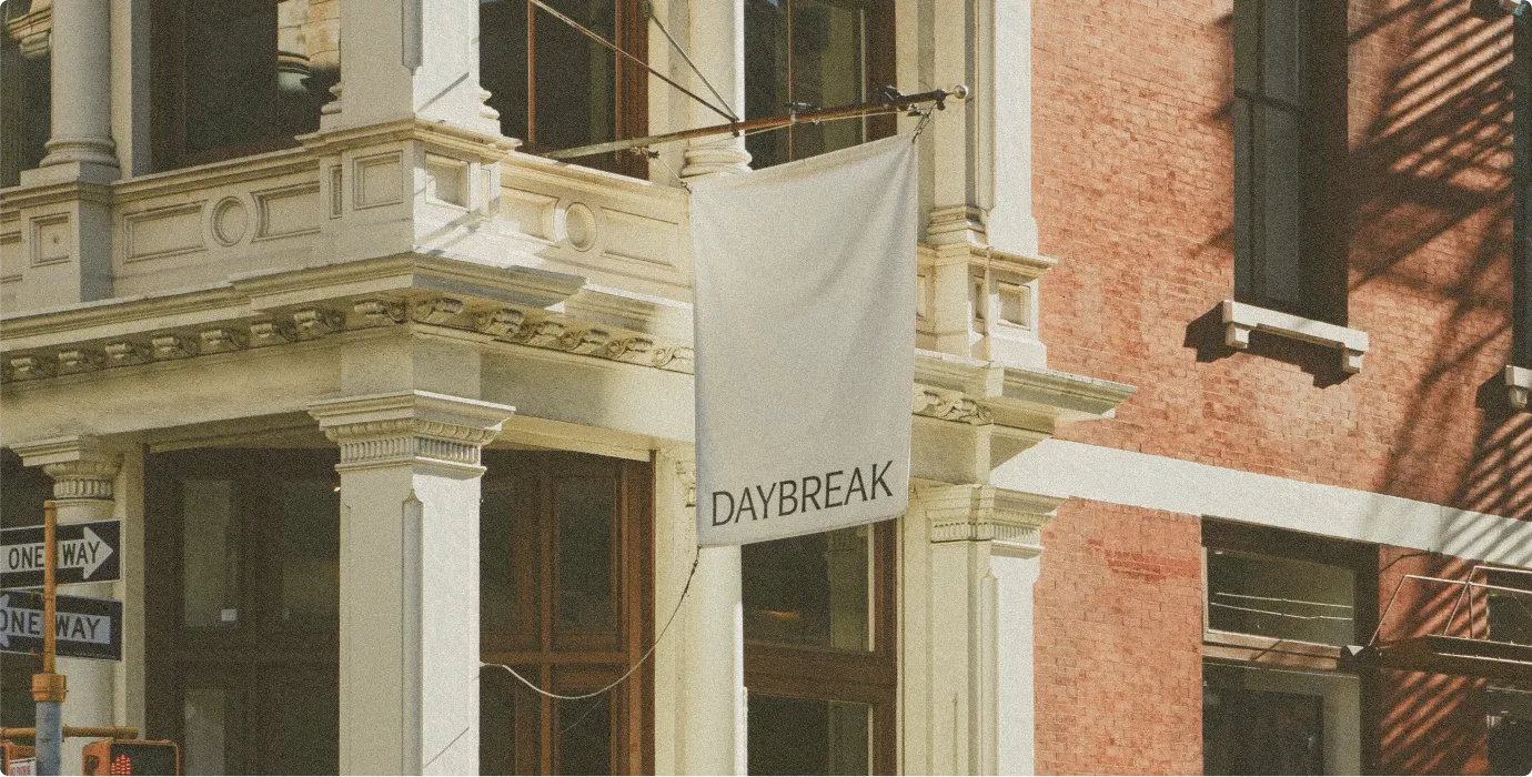 White flag with text 'DAYBREAK' hanging on classic stone building corner in city street.