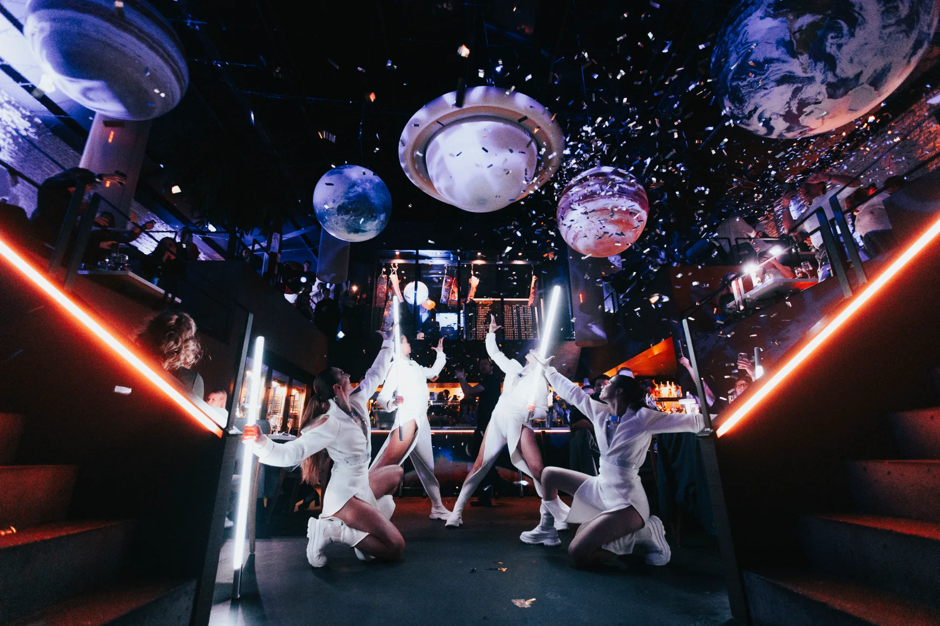 Dancers in white costumes under planet-shaped decor and falling confetti at the Maven Lost in Space New Year's Eve party