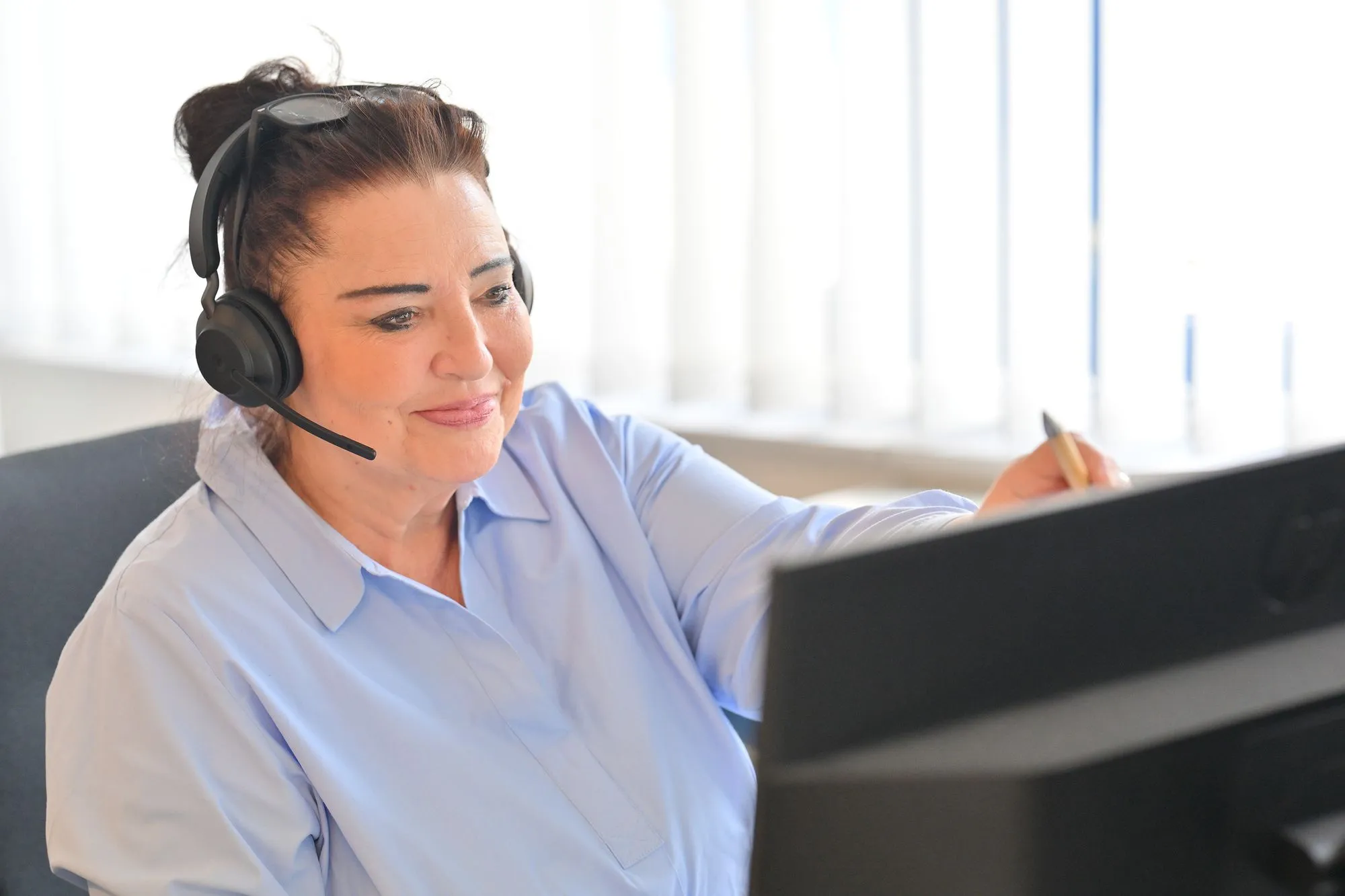 Frau mit Headset, die auf einen Monitor schaut.