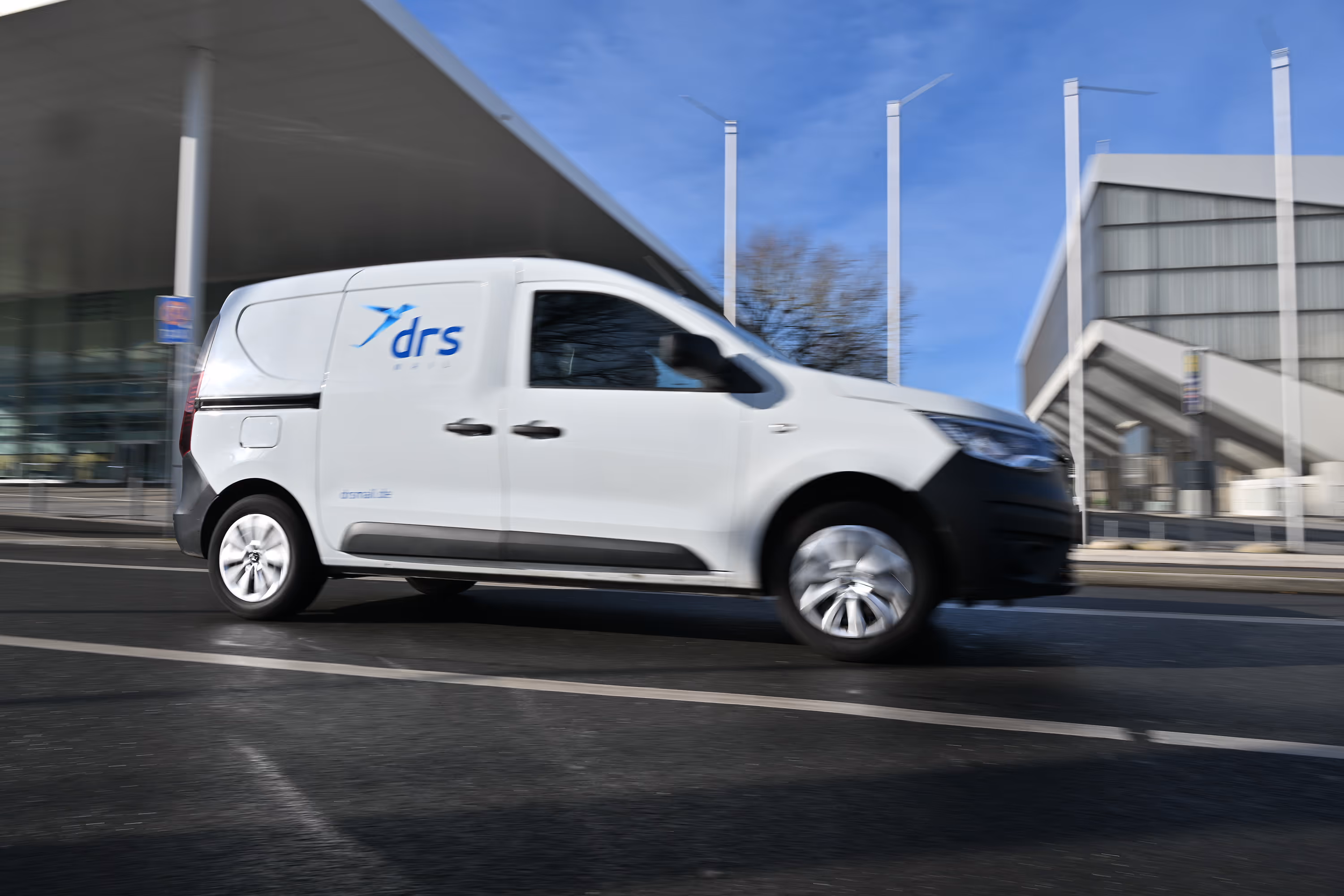 Transportfahrzeug von der drs Mail, das vor einem Gebäude entlangfährt.