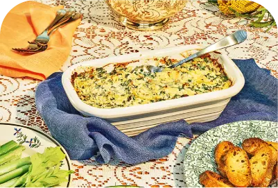 Baked spinach artichoke dip in a white dish with a serving spoon on a blue napkin on a lace tablecloth.