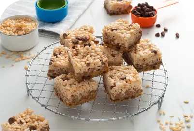 Stack of crispy rice treats with chocolate chips on a round wire rack on a white surface.