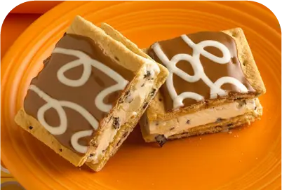 Two chocolate-topped ice cream sandwiches with white swirls on orange plate.