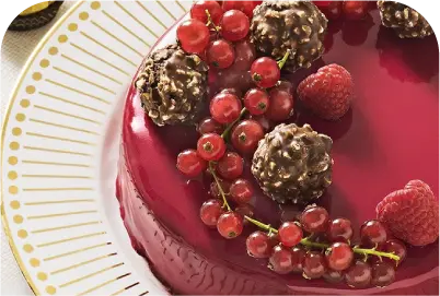 Glossy red berry cake topped with chocolate clusters, red currants, and raspberries on a white plate.