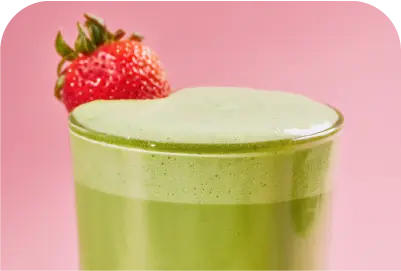 Glass of frothy green matcha tea with a fresh strawberry garnish on the rim against a pink background.