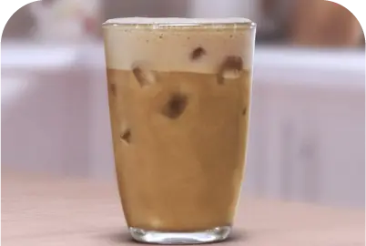 Glass of iced coffee with creamy foam on top on a countertop.