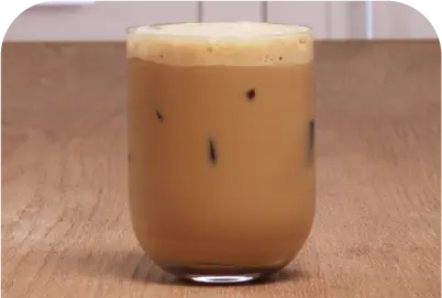 Glass of iced coffee with foam on top on a wooden surface.