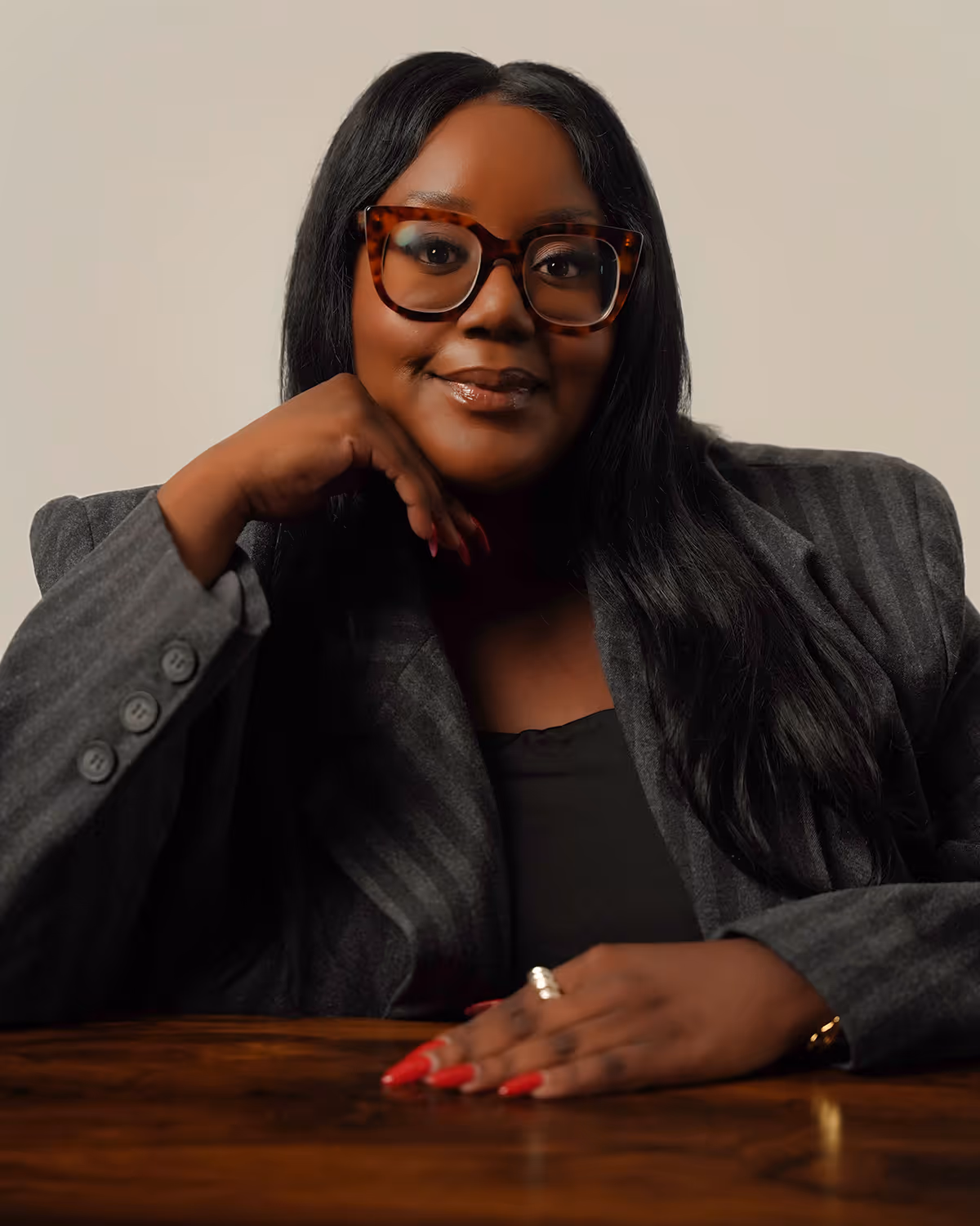 Confident woman with long black hair wearing large tortoiseshell glasses and a gray blazer.