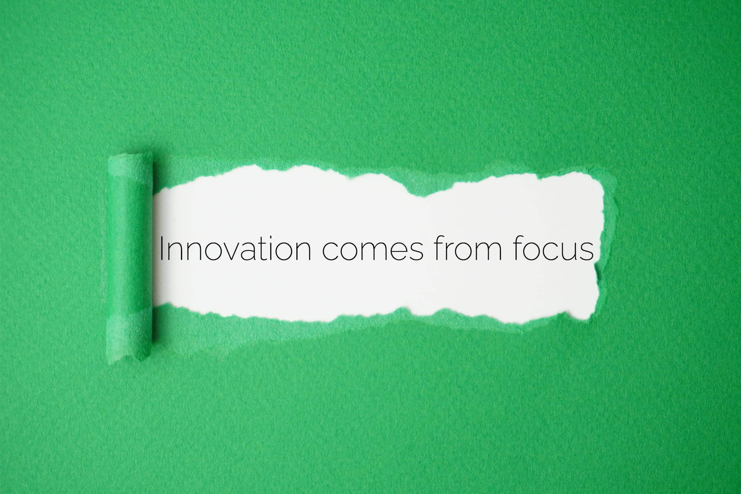 Green paper torn to reveal the words 'Innovation comes from focus' on a white background.
