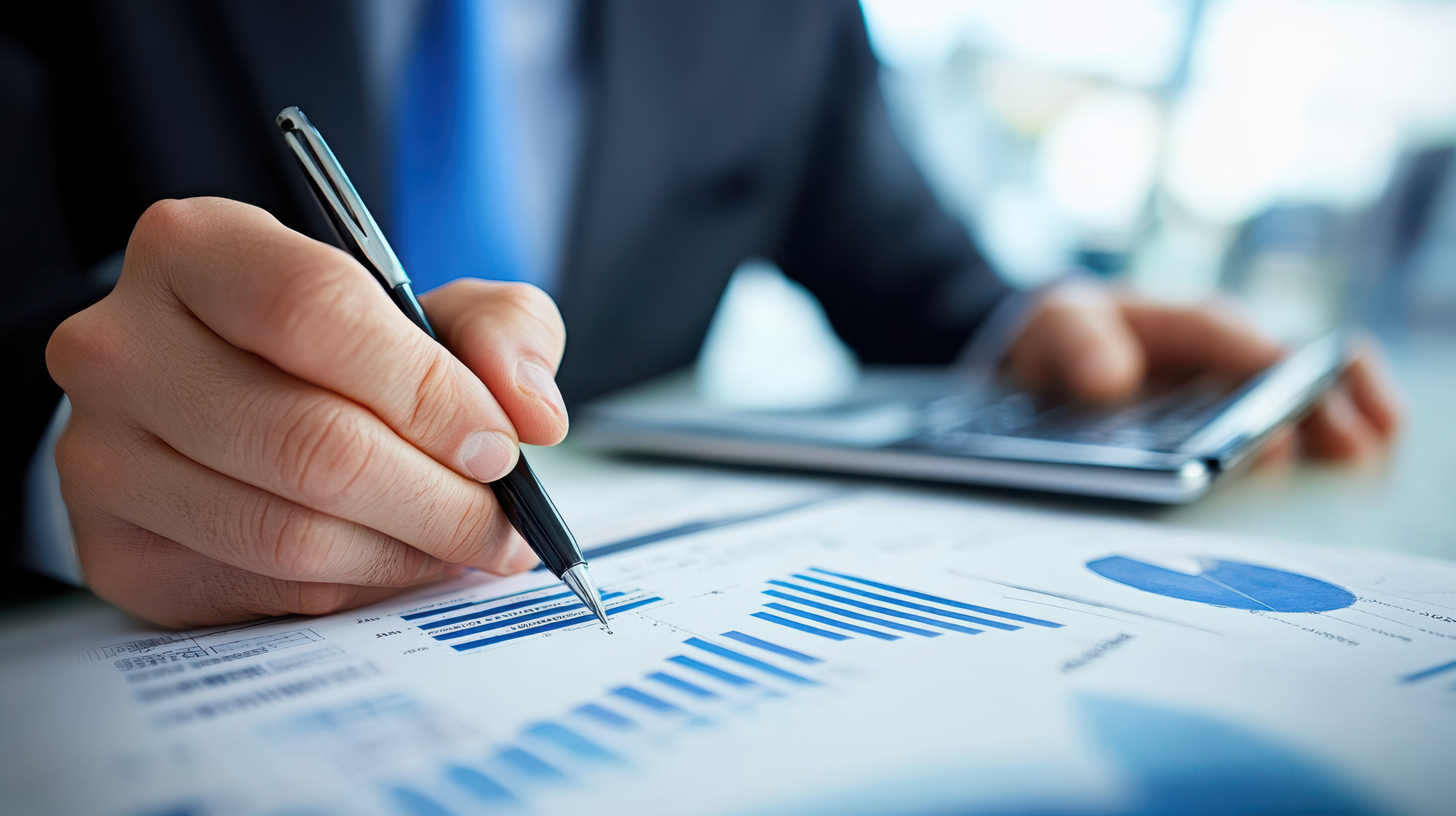 Person in suit reviewing blue bar and pie charts on paper while using a calculator.
