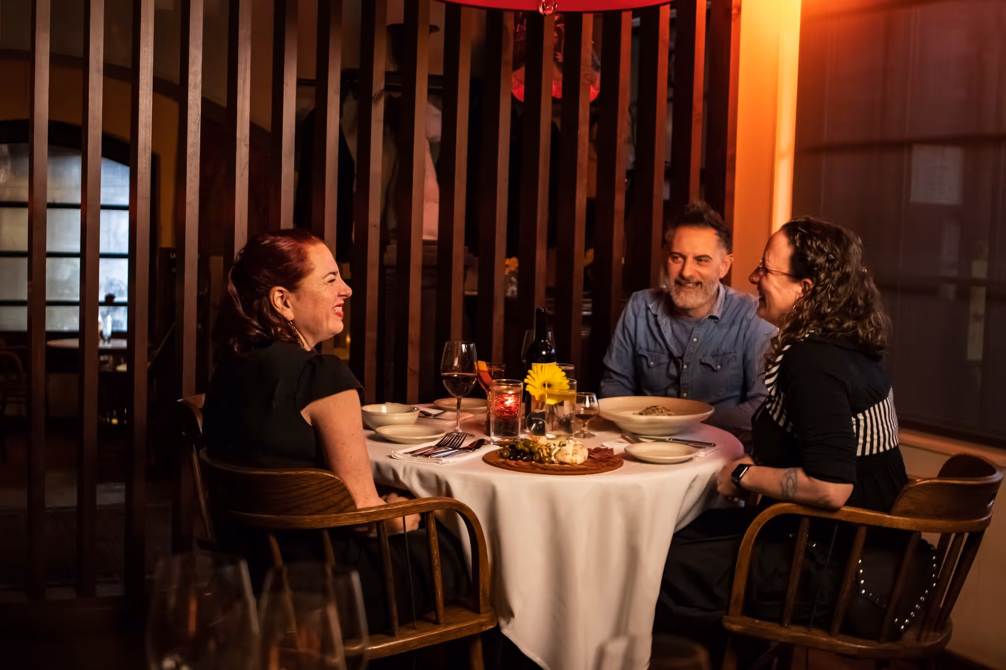 A group of people sitting around a table with wine glasses and plates of food.