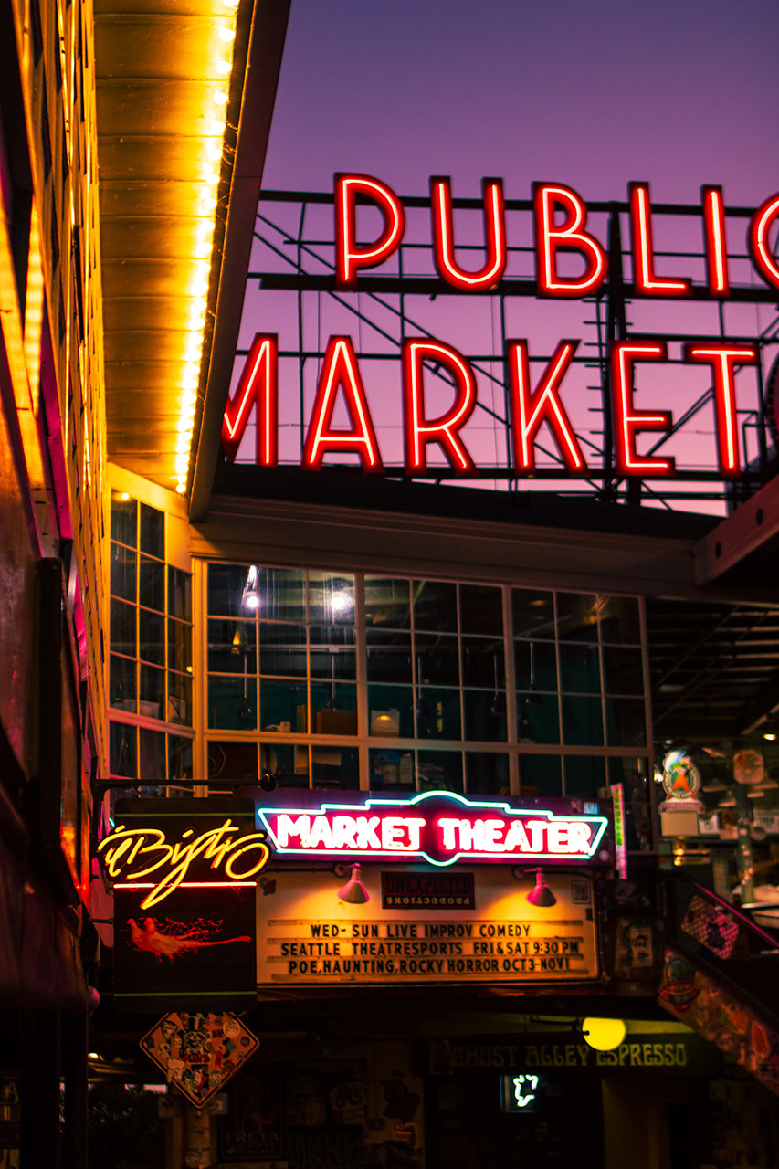 Neon signs for Public Market and Market Theater at dusk with purple sky in background.