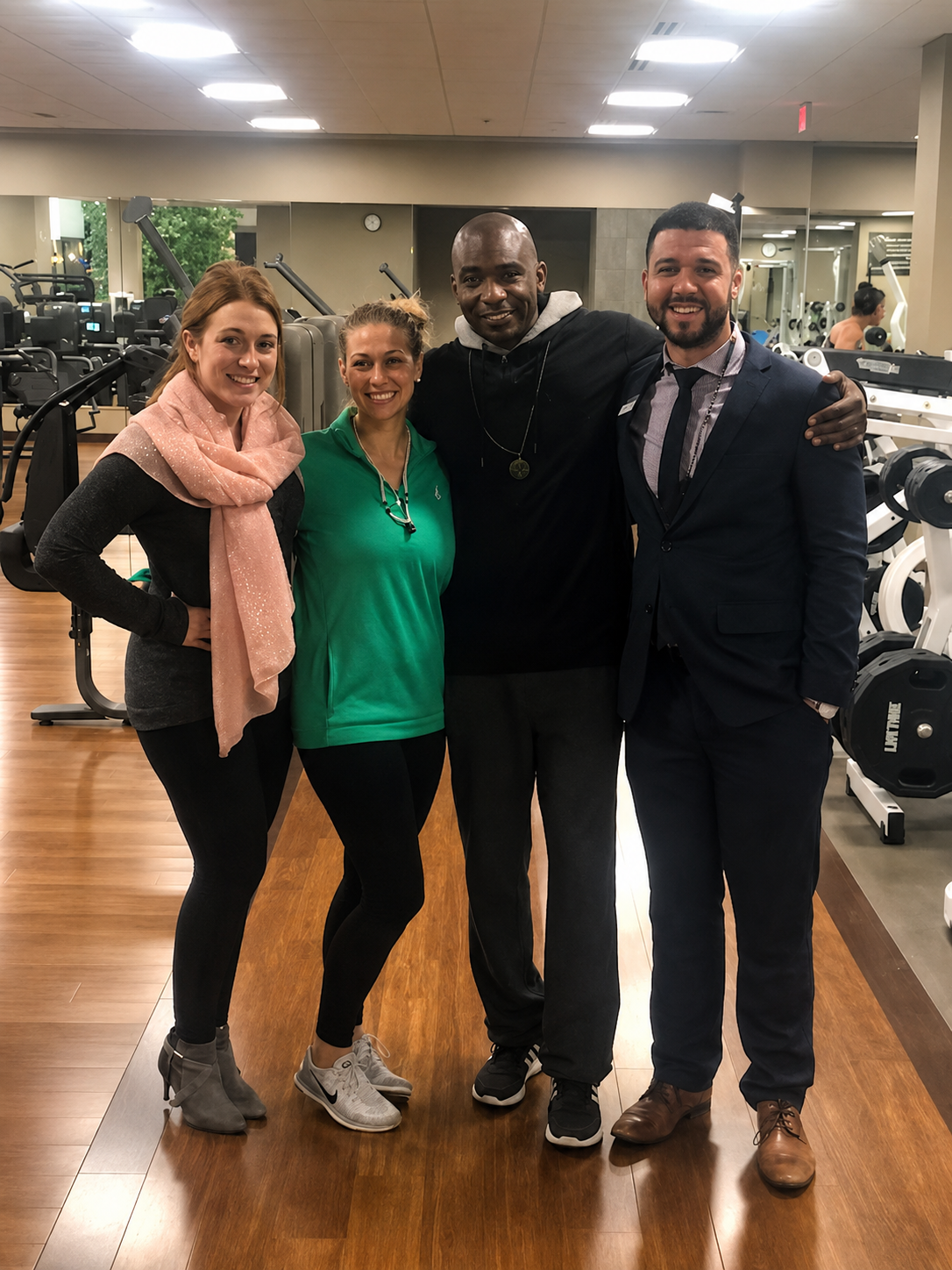 Four people smiling inside a gym, with workout machines and mirrors in the background.