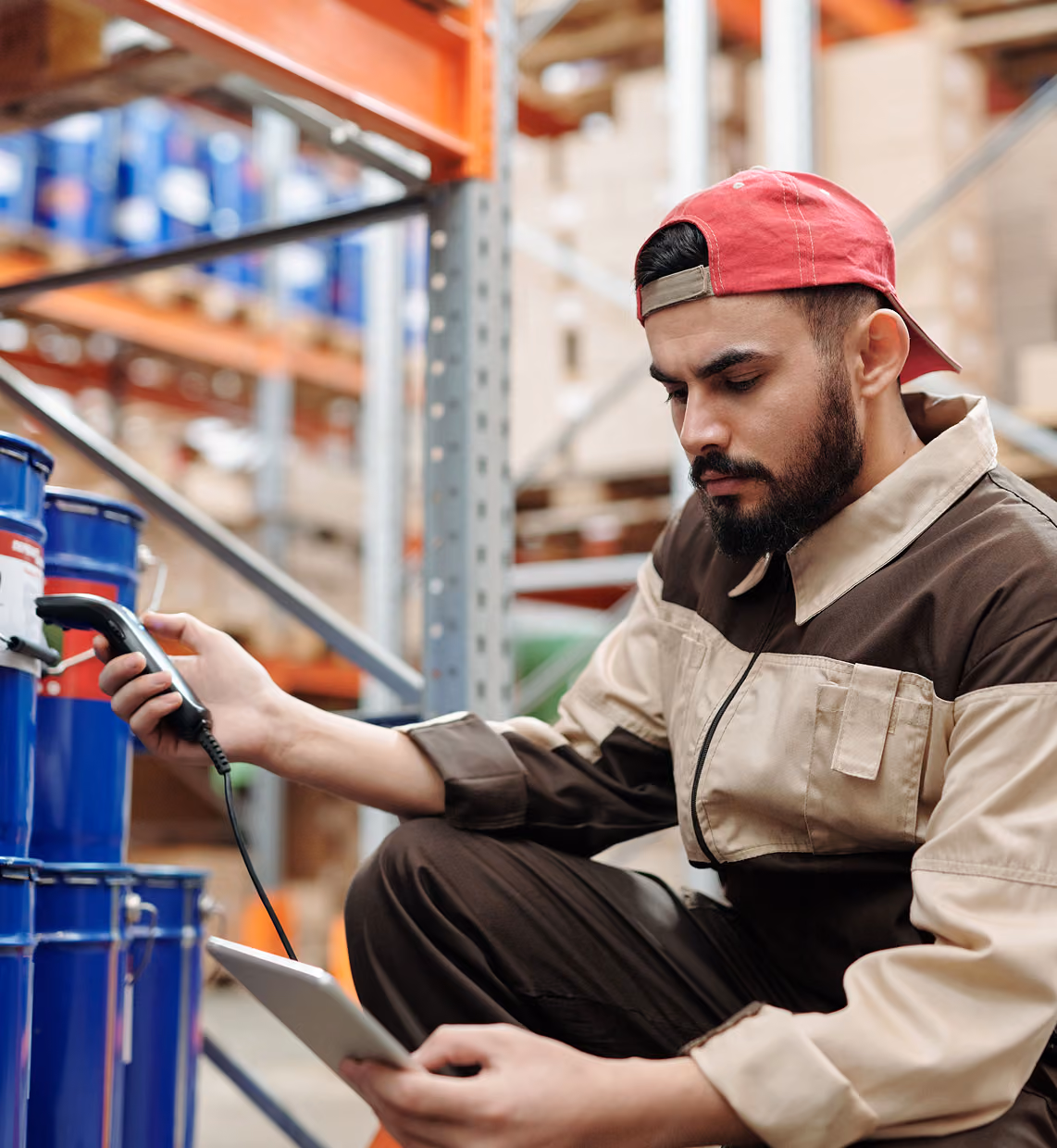 Warehouse worker scanning blue barrels with a handheld device while holding a tablet.