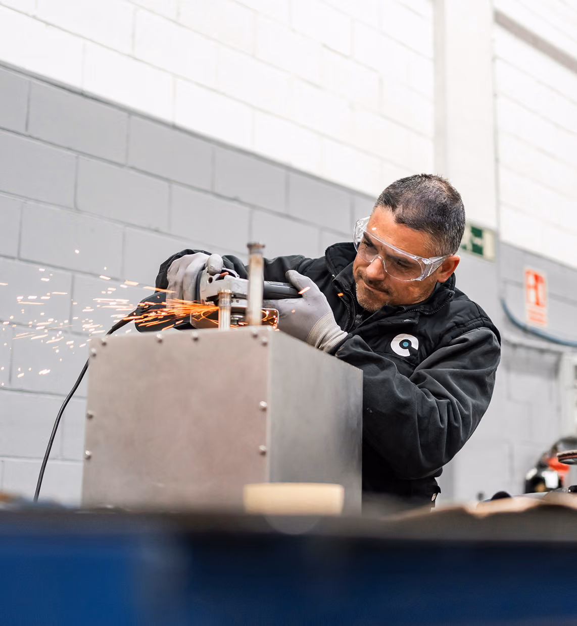 Man wearing safety glasses using an angle grinder on metal with sparks flying in a workshop.