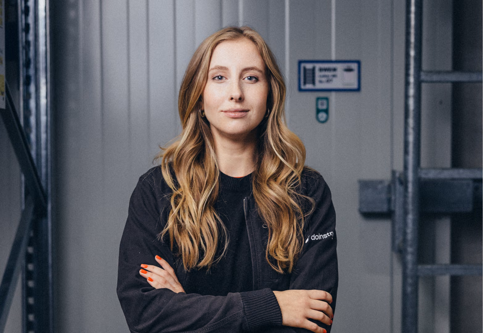 Portrait of a confident woman with long blonde hair wearing a black jacket with crossed arms.