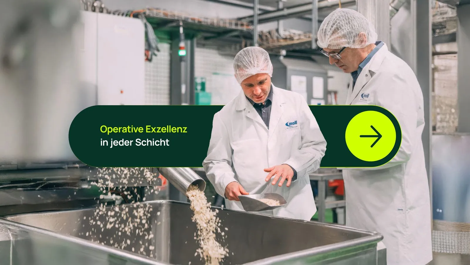 Two men in white lab coats and hairnets working with grains in a food processing facility.