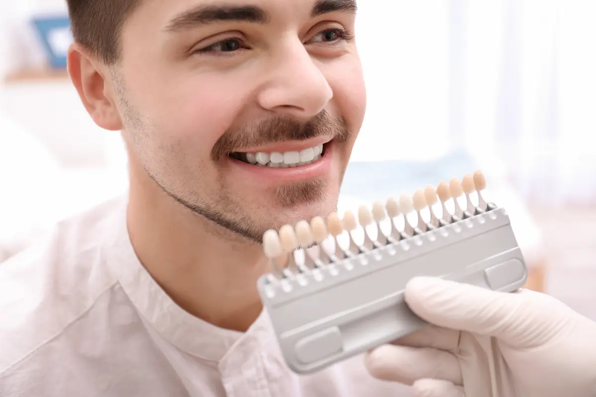 Smiling man at DTC Dental Treatment Center in Richmond, BC, comparing teeth color with a