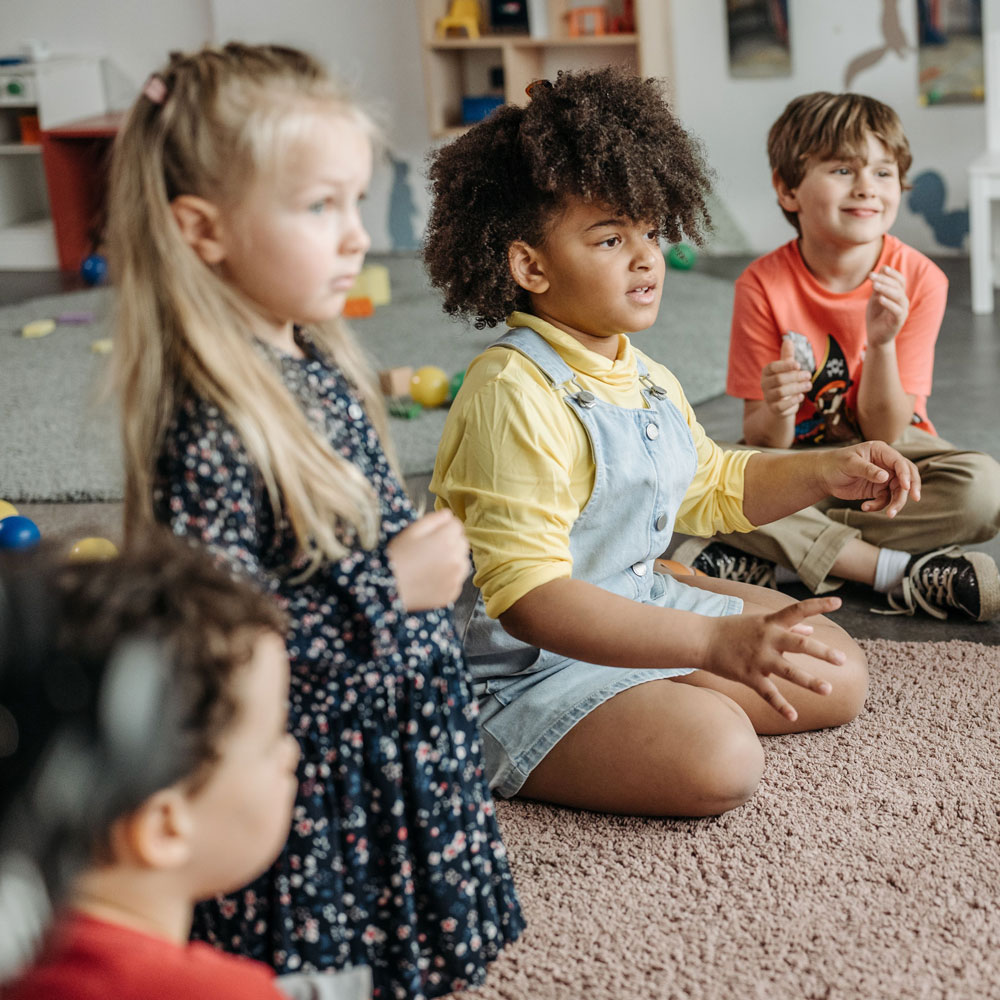 Four children sitting on the floor in a classroom setting, engaging in a group activity.