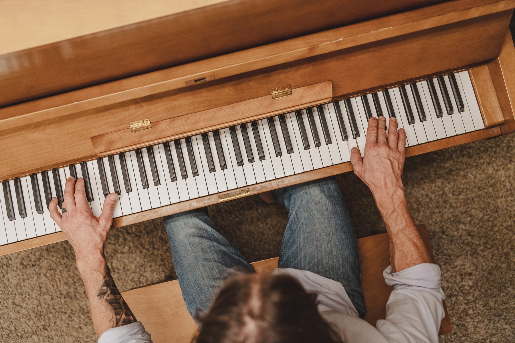 Overhead view of a person playing a wooden piano with both hands on the keys.