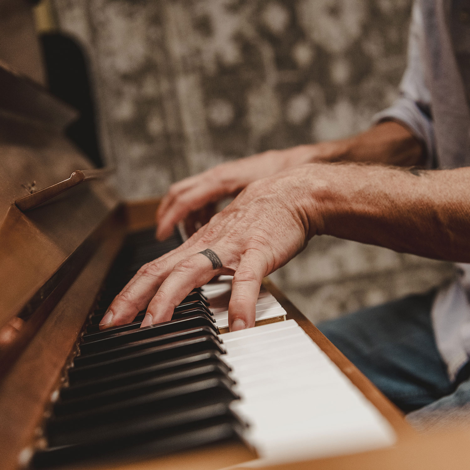Close-up of hands playing piano keys, one hand with a black ring tattoo on finger.