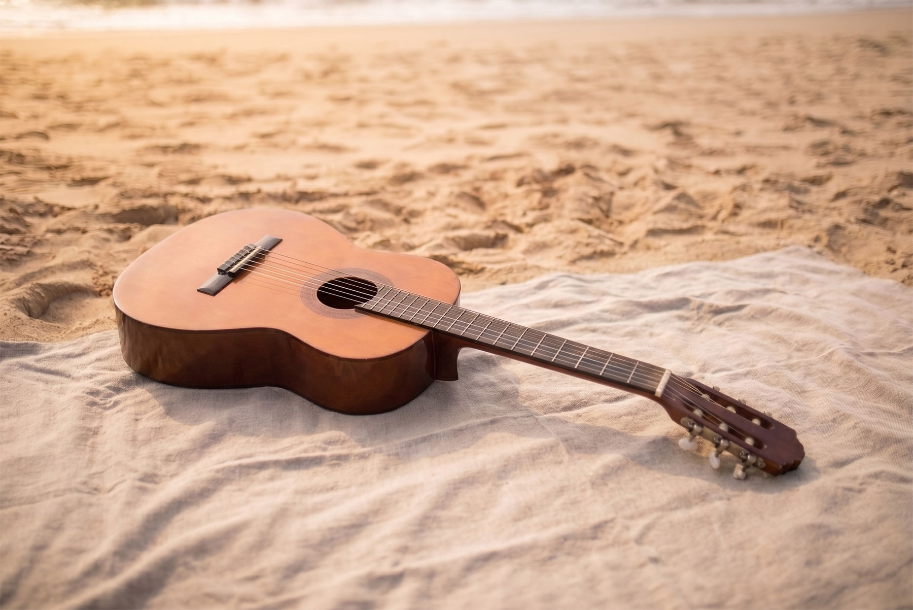 Acoustic guitar lying on a cloth on sandy beach at sunset or sunrise.