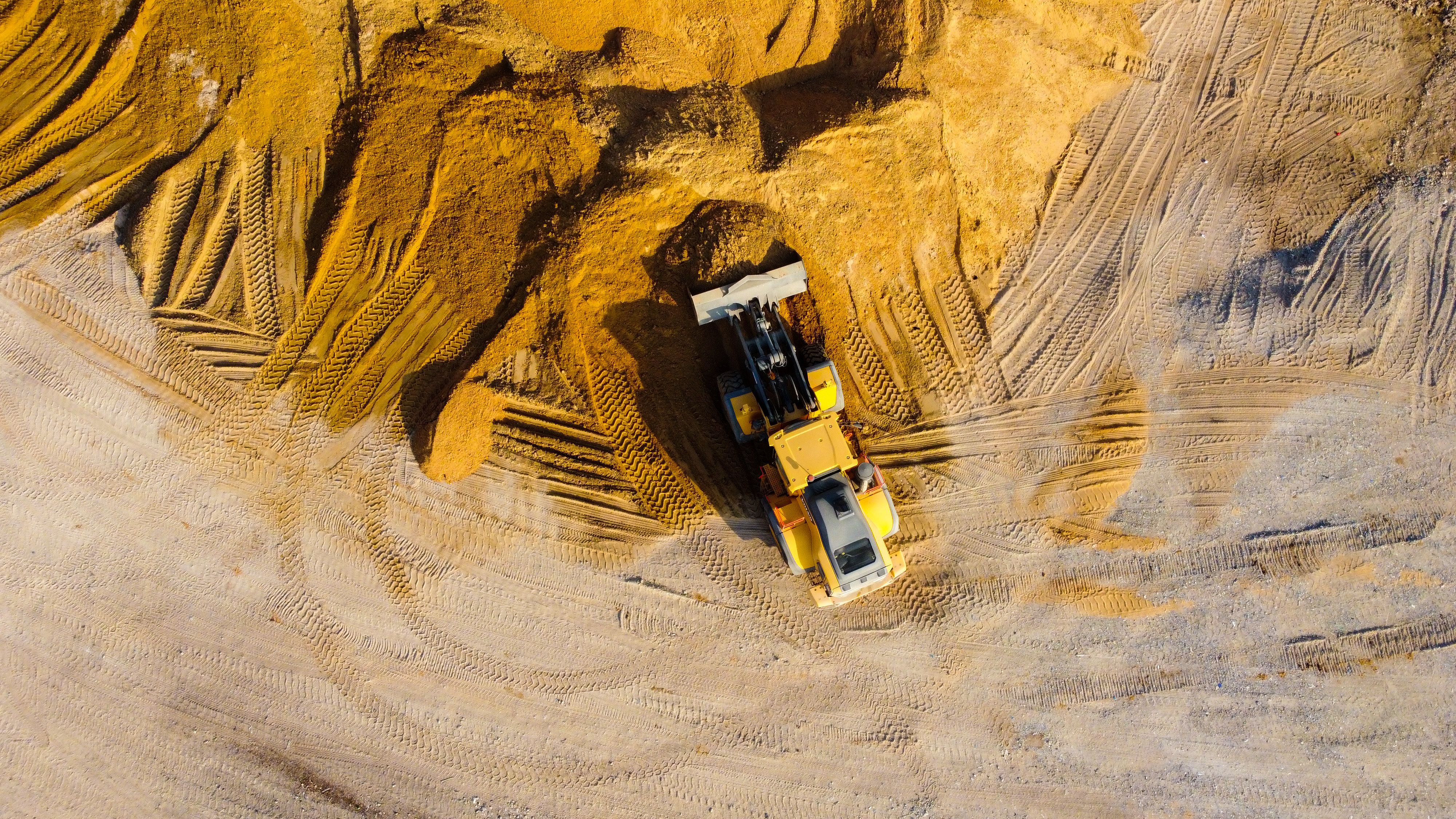 A yellow bulldozer clearing and shaping soil at a construction site with visible tire tracks.
