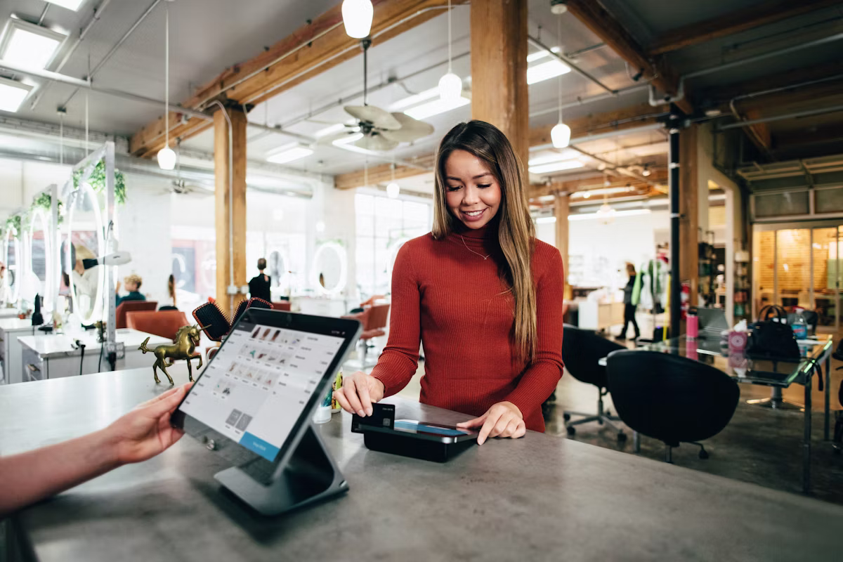 Smiling woman in a red sweater making a card payment at a store counter with a modern POS system.