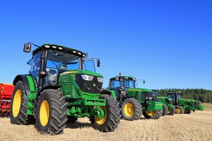 Row of green and yellow tractors on a dry field under a clear blue sky.