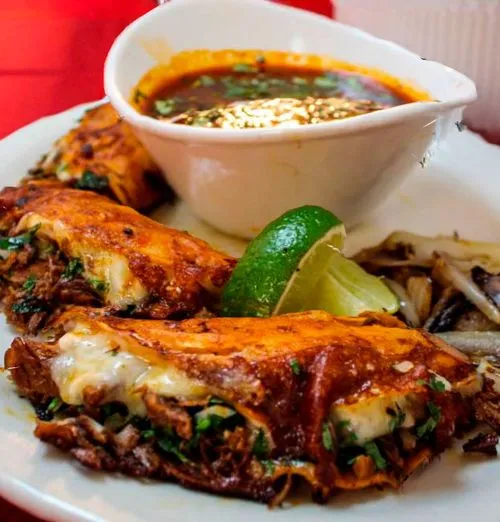 A couple quesabirria slices with birria soup and lime