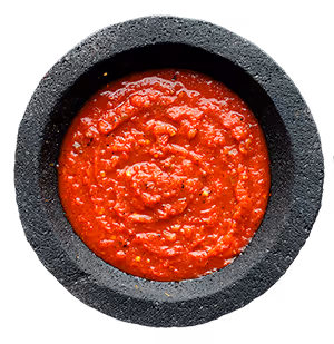 Black stone bowl filled with red salsa sauce with visible bits of ingredients.