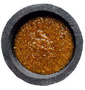 Stone bowl filled with chunky green chili salsa with visible seeds and herbs.