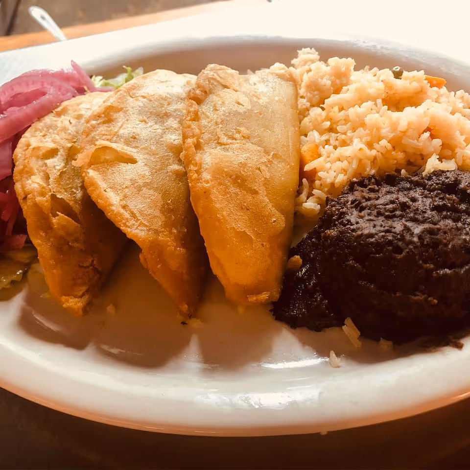 Plate with three golden empanadas, seasoned rice, black beans, and pickled red onions.