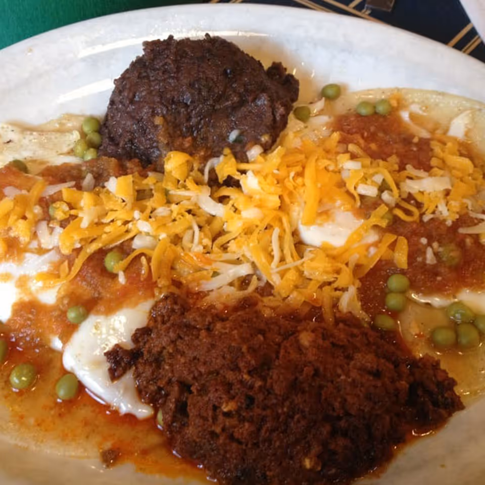 Plate with two fried eggs topped with shredded cheese, hot sauce, peas, and two sausage patties.