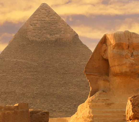 Close-up of the Great Sphinx with a pyramid in the background at sunset in Egypt.
