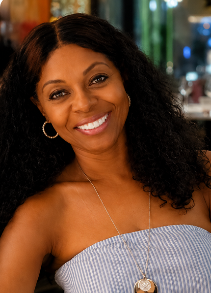 Smiling woman with curly hair wearing hoop earrings and a striped strapless top with pendant necklace.