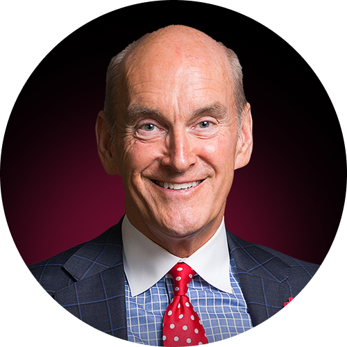 Smiling bald man wearing a checkered blue shirt, red polka dot tie, and dark suit jacket.