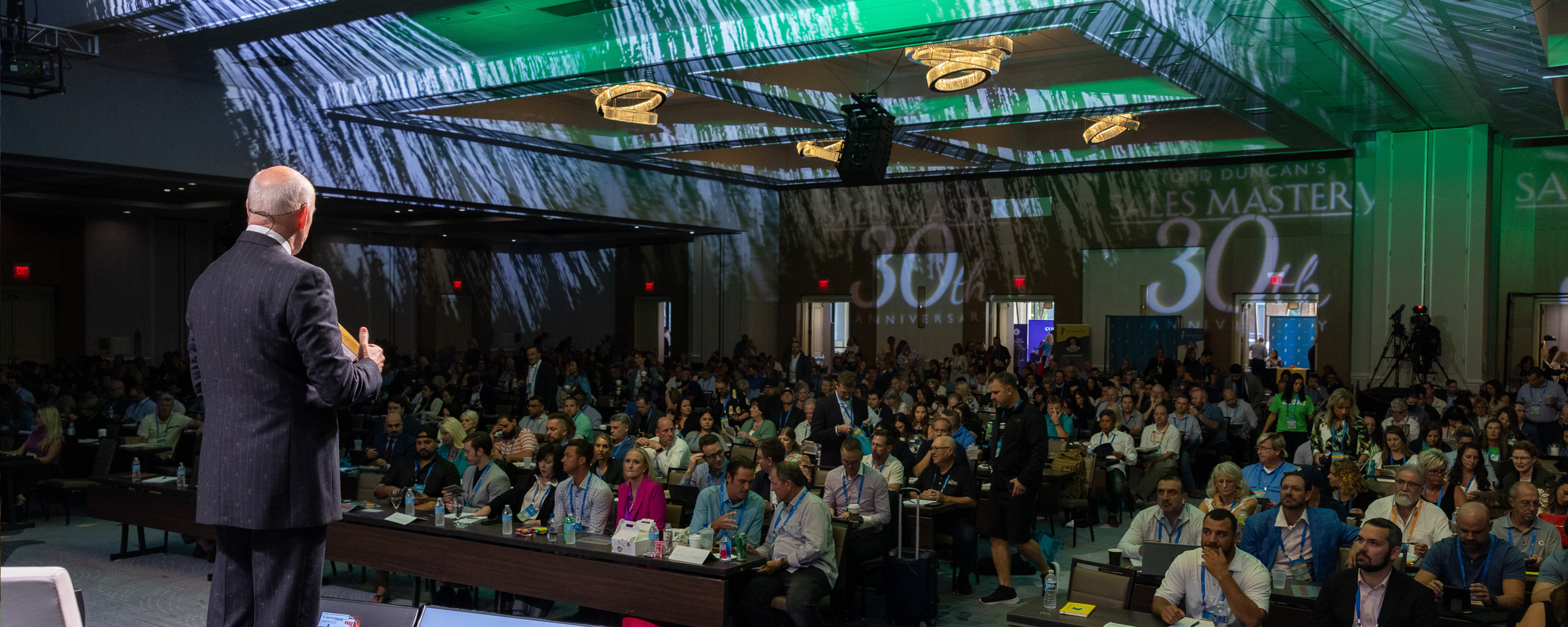Speaker addressing an audience at Todd Duncan's Sales Mastery 30th Anniversary event in a large conference room.