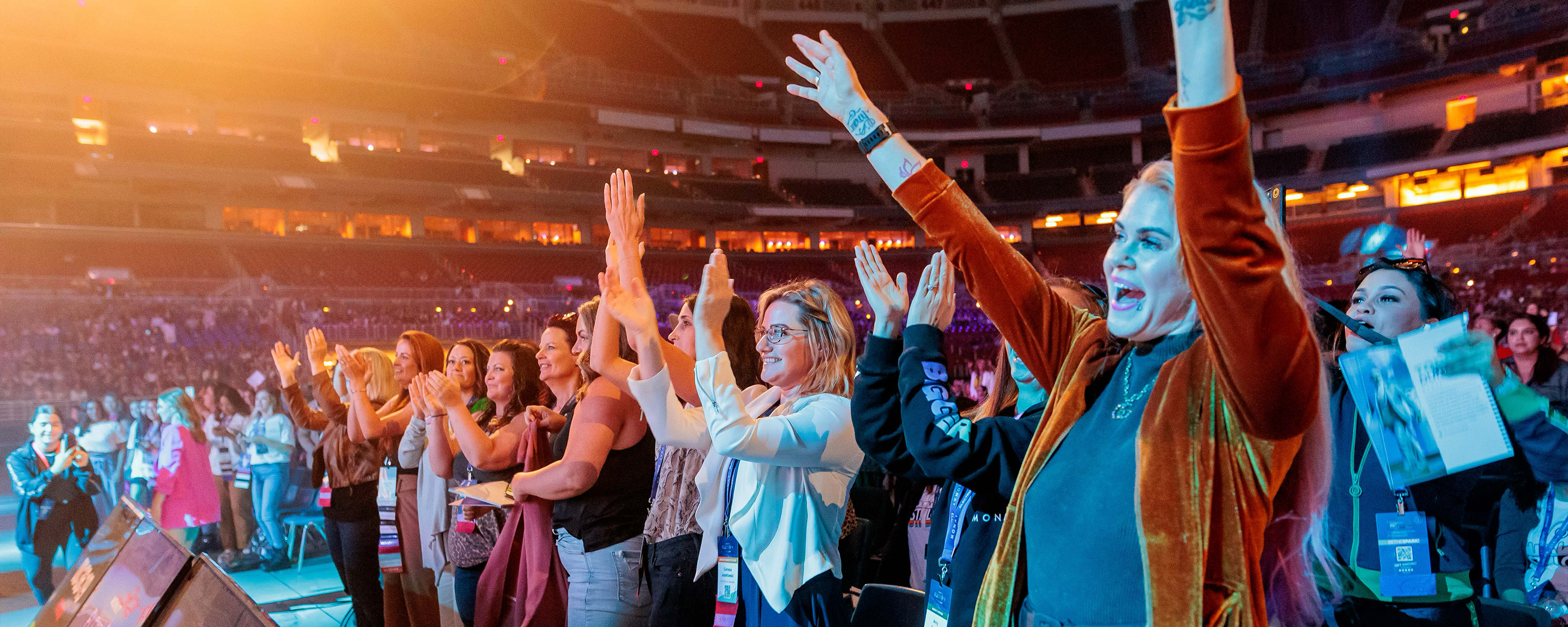 Audience members cheering and clapping energetically at a large indoor event or concert.