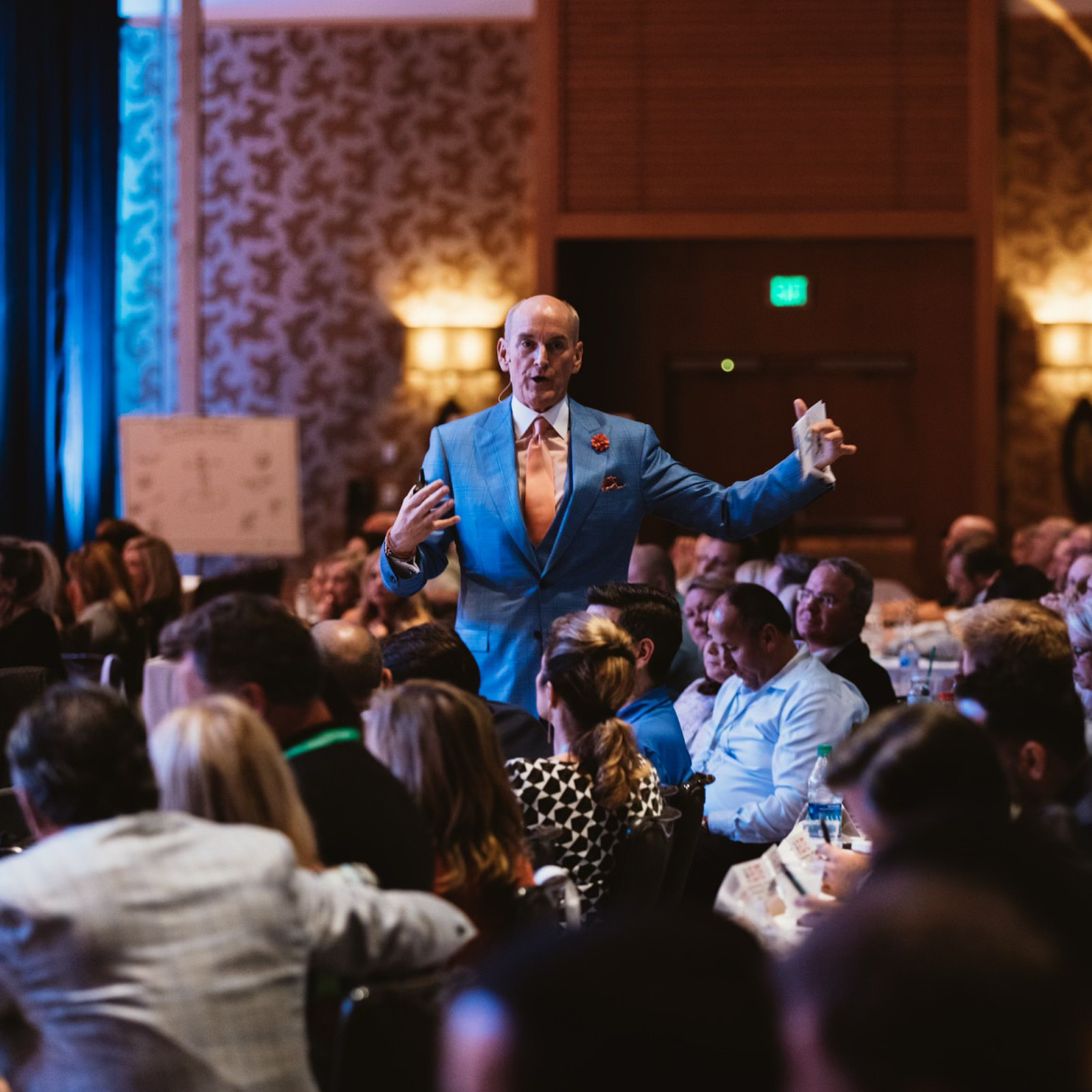 Man in blue suit speaking to a seated audience in a conference room.
