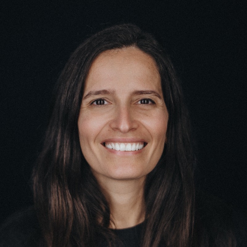 Woman with long brown hair smiling against a black background.