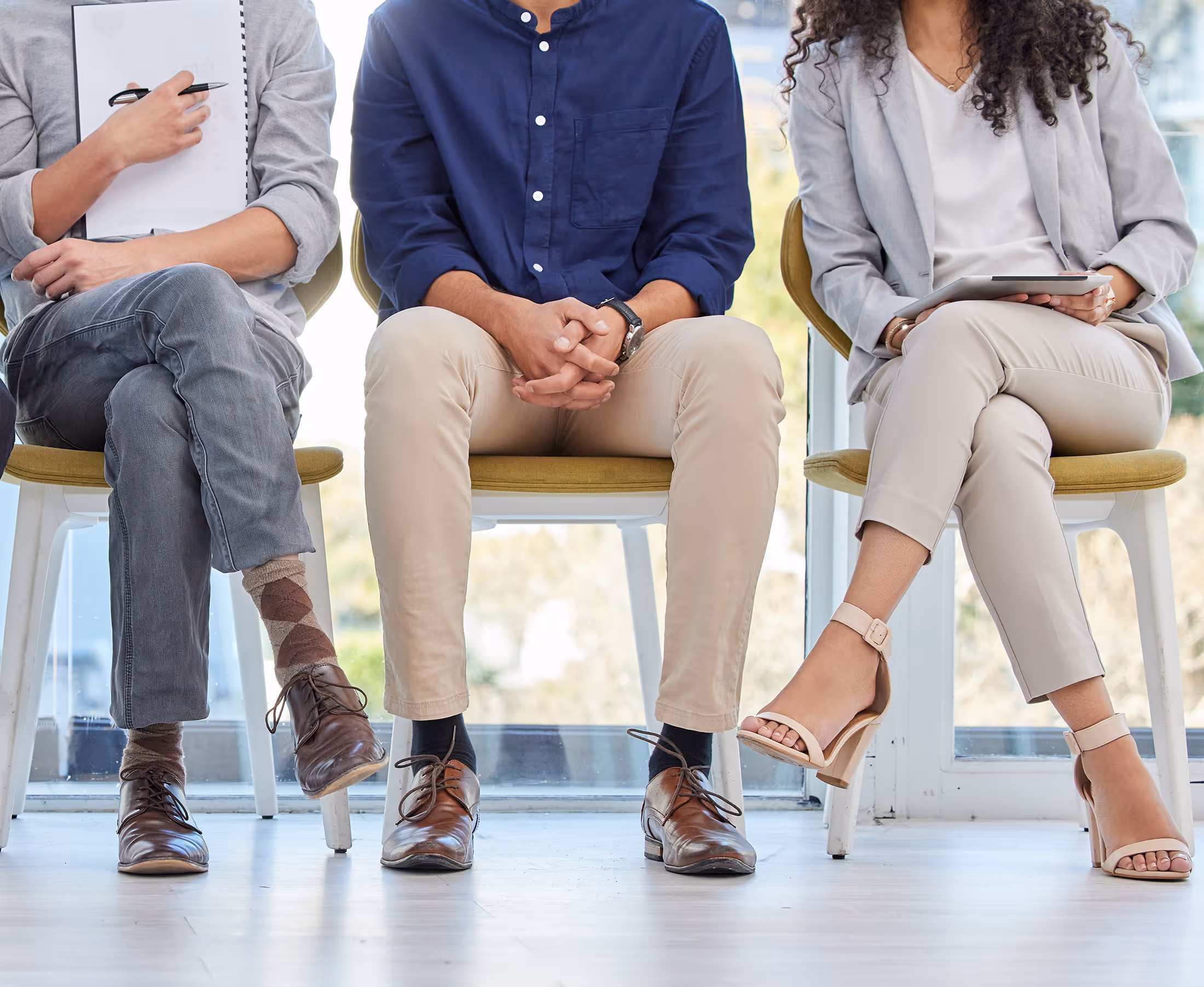 Three people sitting with crossed legs, two men with dress shoes and a woman with beige heels.