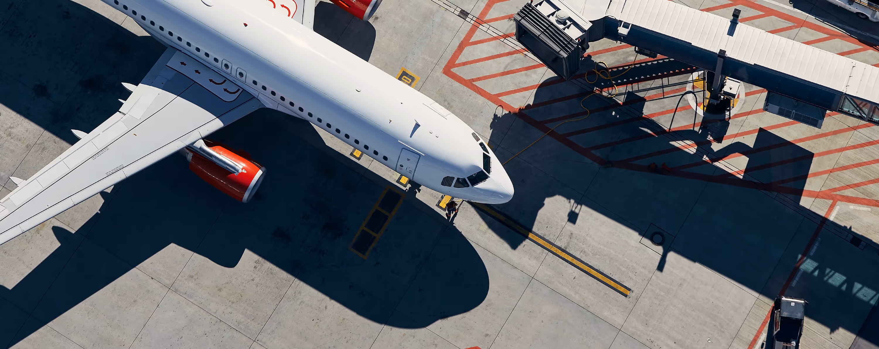 Top-down view of a white commercial airplane with red engines parked next to a jet bridge on the tarmac.