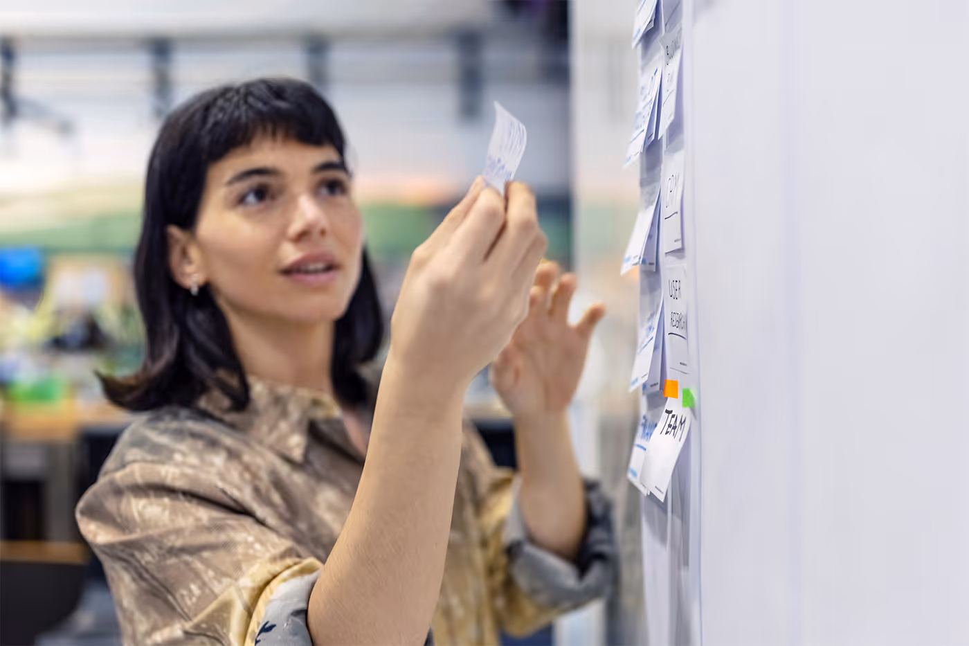 Woman placing sticky notes on a whiteboard with a blurred office background.