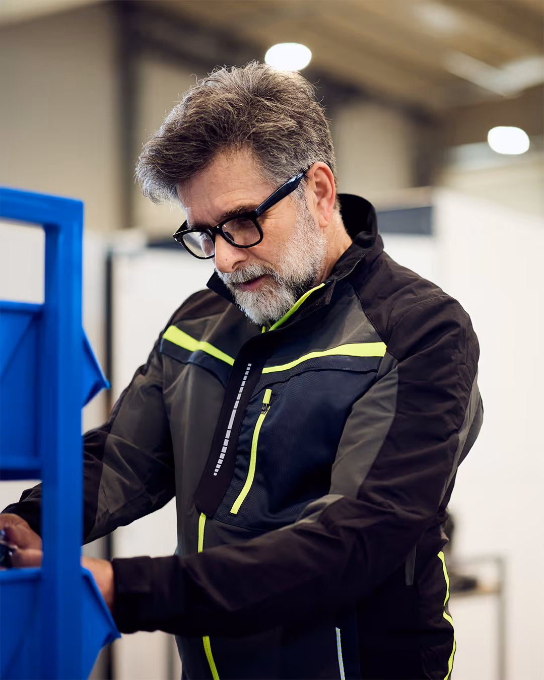 Man with gray hair and beard wearing glasses and a jacket working with a blue shelving unit.