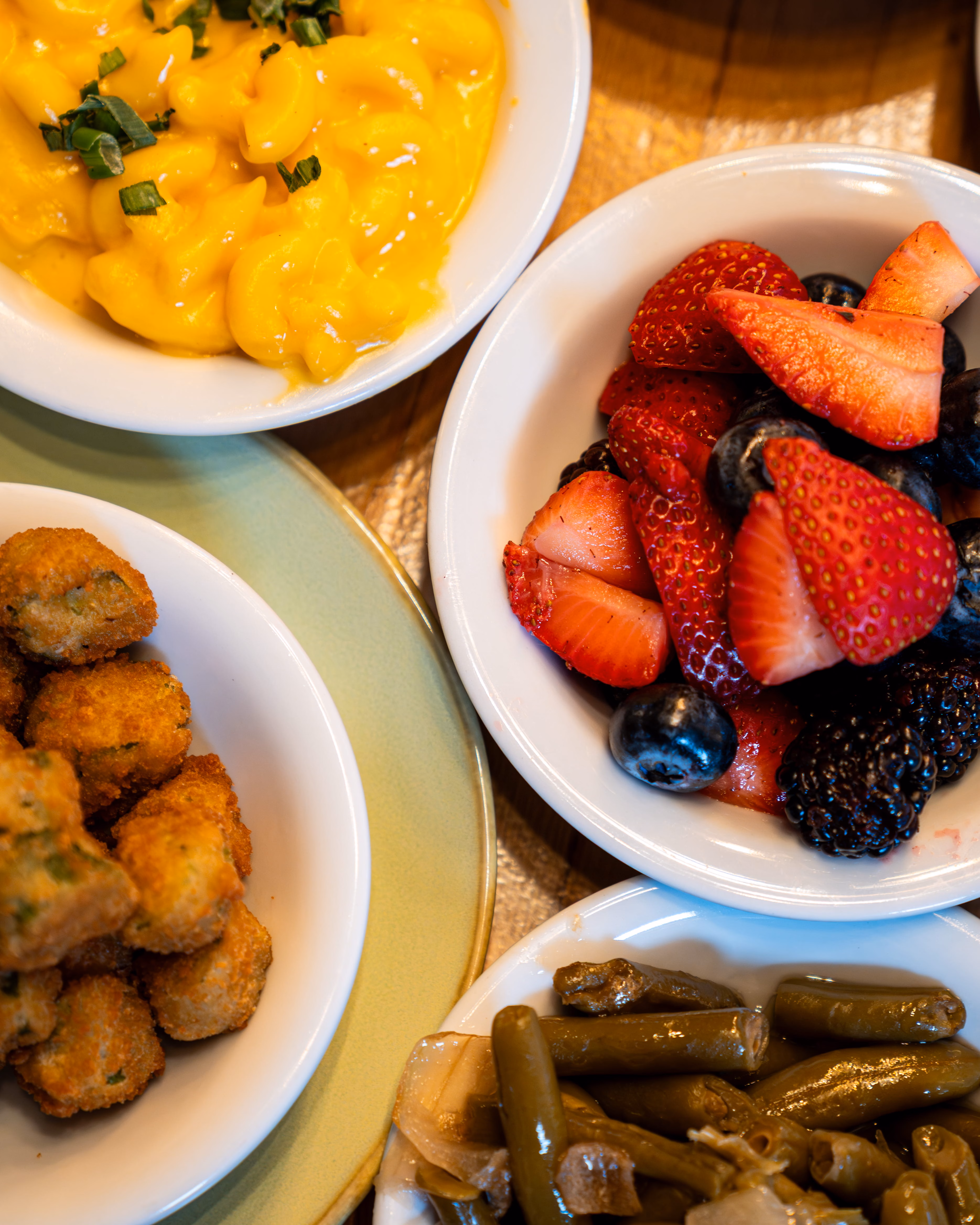 A vibrant display of comfort food: creamy mac and cheese, a fresh fruit salad of strawberries and berries, crispy fried bites, and seasoned green beans.