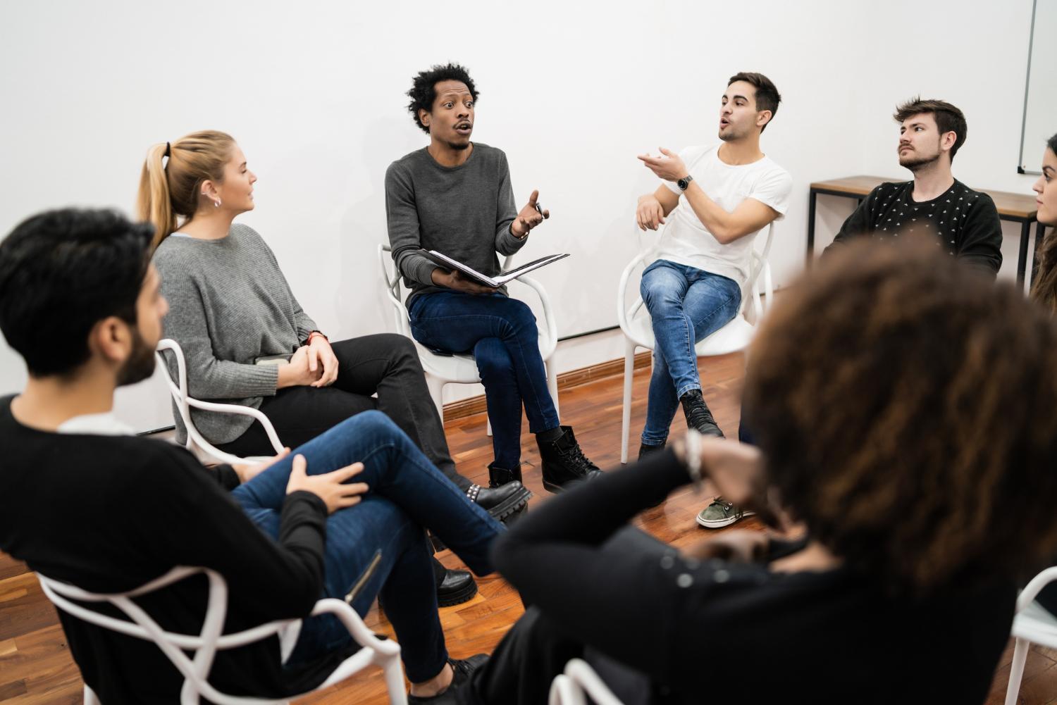 La imagen muestra a un grupo de personas sentadas en sillas colocadas en forma de círculo. Estas personas parecen estar discutiendo asuntos importantes en una reunión de trabajo.
