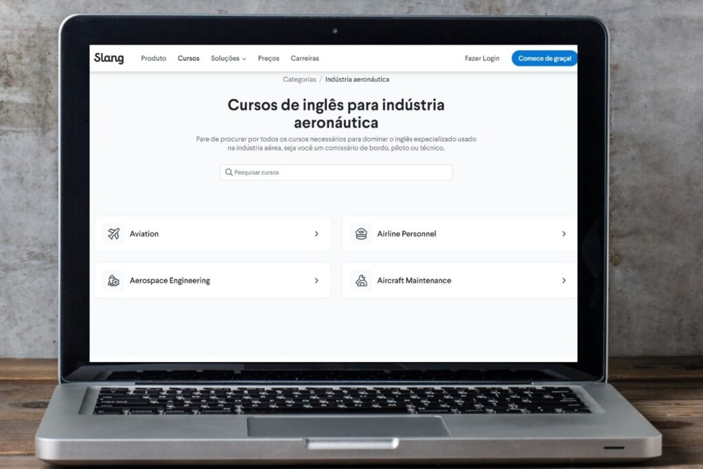 Um laptop prata está sobre uma mesa de madeira. Na tela há um print da página de cursos de inglês para aeronáutica.